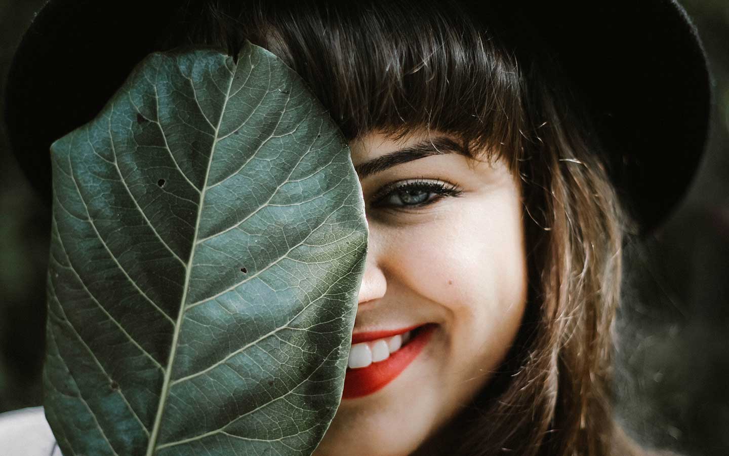 Uśmiechnięta kobieta chowająca się za zielonym liściem